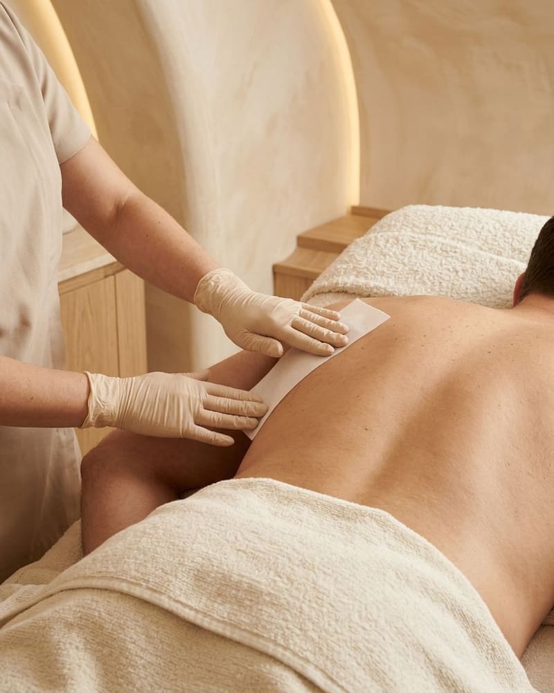 Gloved hands applying a wax strip along a man's bare back